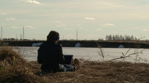 Girl using laptop sitting back to camera, listening music in blue headphones. Video stock 75686485