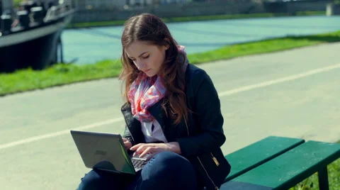 Girl using laptop while sitting on the bench and smiling to the camera Vídeos de archivo 66524678