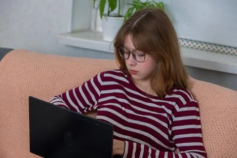 Girl using laptop while sitting on sofa in a cozy room with plants, focusing  Foto stock