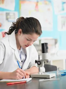 Girl Using Microscope And Taking Notes Stock Photos