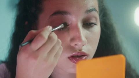 Girl using a mirror to apply eye shadow Stock Footage 275013598