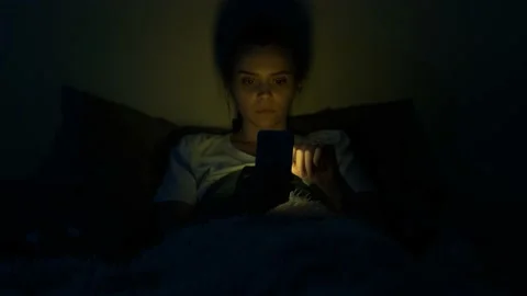 Girl using mobile phone lying in bed at night. Young woman browsing online Stock Footage 140516137