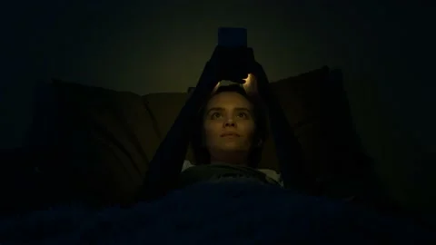 Girl using mobile phone lying in bed at night. Young woman browsing online Stock Footage 140579683
