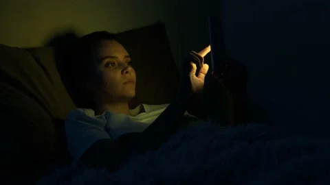 Girl using mobile phone lying in bed at night. Young woman smiling browsing Stock Footage 140579749