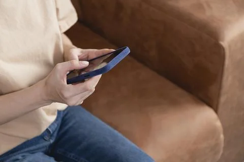 Girl using mobile phone while sitting on couch in living room, closeup. Stock Photos