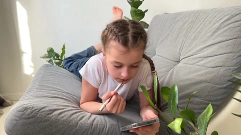 Girl using phone apps looking at mobile device while sitting on sofa, teenager 스톡 동영상 238598051