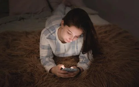 Girl Using Phone While Lying on Bed in Evening Light Fotos Stock
