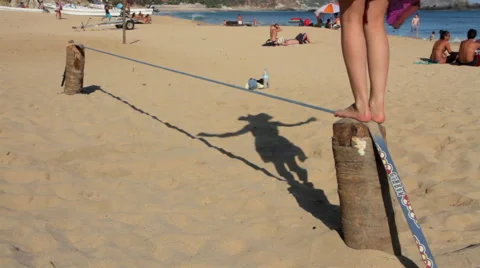 Girl using a slackline in the beach, her shadow projected in the sand. Stock Footage 49762548