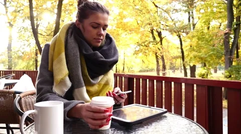 Girl using smartphone and drinking coffee. Tablet pc on the table. Autumn time Stock Footage 56546736