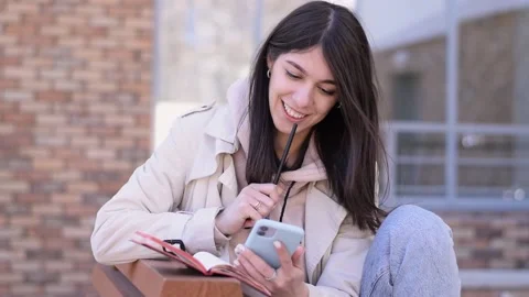 Girl using a smartphone and making notes in a notebook on a street bench Stock Footage 152710163