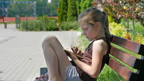 Girl is using smartphone on a bench in park Stock Footage