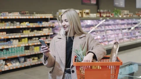 Girl using smartphone while shopping at a food market filled Video stock 301544711