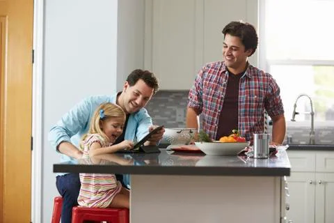 Girl using tablet computer in kitchen with her male parents Stock Photos