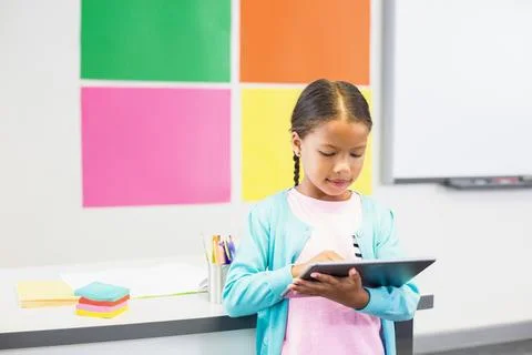 Girl using tablet in elementary classroom showing colorful paper panels and Stock Photos
