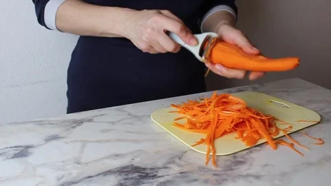 Girl using a vegetable peeler cuts carrots for salad into thin strips Stock-Footage 308101721