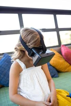 Girl using virtual reality headset while sitting on couch in school library Stock Photos