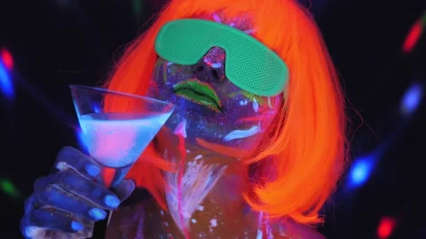 A girl with an UV pattern on her face in an orange wig and green glasses dances. Stock Footage 145960598