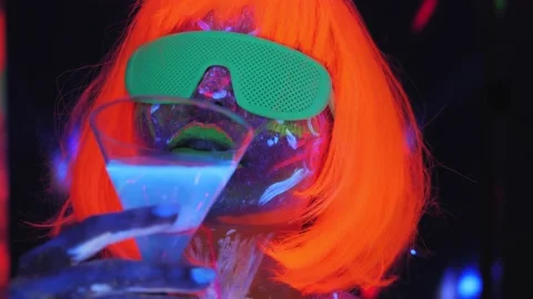 A girl with an UV pattern in an orange wig and glasses with a Martini glass. Stock Footage 221342224