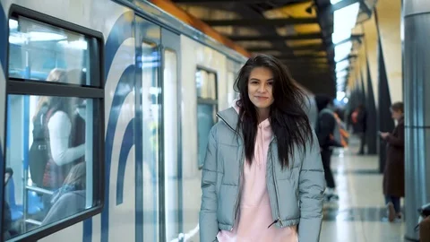 Girl waiting for a passing train the metro station laughs, looks at the camera Stock Footage 125919082