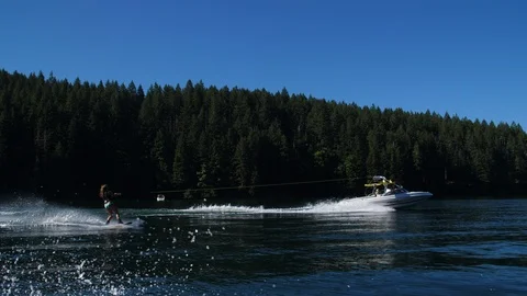 Girl on Wakeboard Pulled Behind Boat Surrounded by Evergreen Trees Stock Footage 102401047