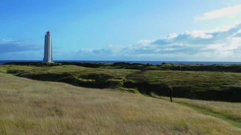 Girl walking the grass path to the lighthouse in the field on a cliff of Iceland Stock Footage 168078959