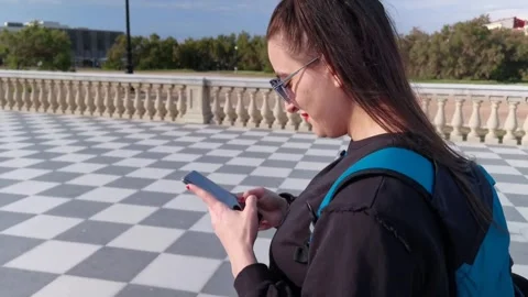 A girl walking on the square while using her smartphone Stock Footage 250186640