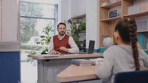 Girl wants to answer a question asked by teacher, stands near the desk. Video stock 162736365