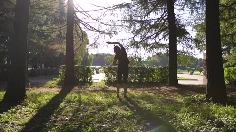 Girl warming up in the park between trees in the morning on a sunny day Stock Footage 138924113