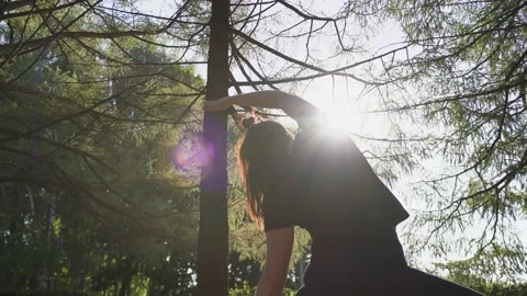 Girl warming up in the park between trees in the morning on a sunny day Stock Footage 138924595