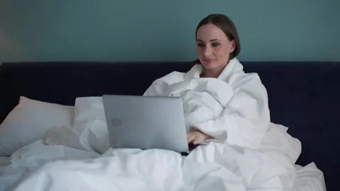 Girl was using a laptop while lying on the bed. A young pretty woman dressed in Stock Footage 252685770