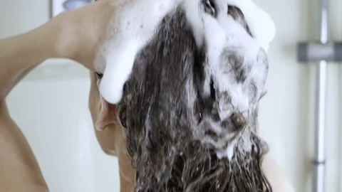 A girl is washing her hair. White foam from the shampoo on long hair brunettes Stock Footage