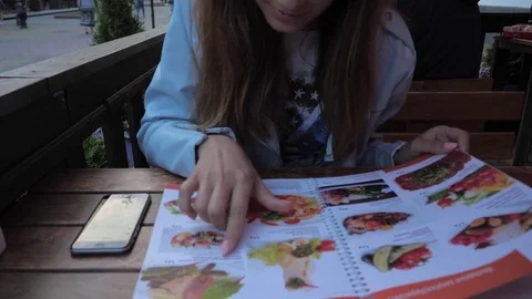The girl is watching the menu to order dinner, is distracted by the phone. Stock Footage 77454067