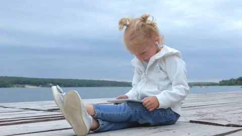 Girl watching at tablet pc while sitting near lake in slow motion Stock Footage 91726264
