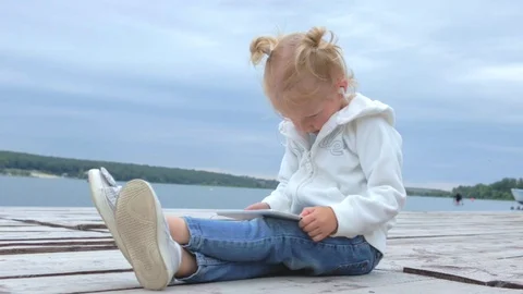 Girl watching at tablet while sitting on wooden pier Stock Footage 91726321