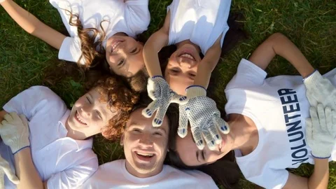Girl waving while group of volunteers relaxing on grass Stock Footage