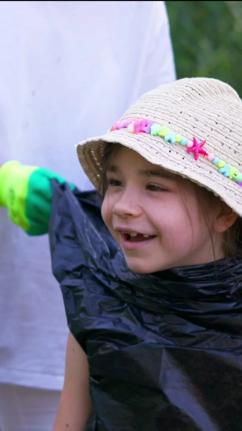 Girl wearing hat carrying black garbage bag on green riverbank Stock Footage 340576953
