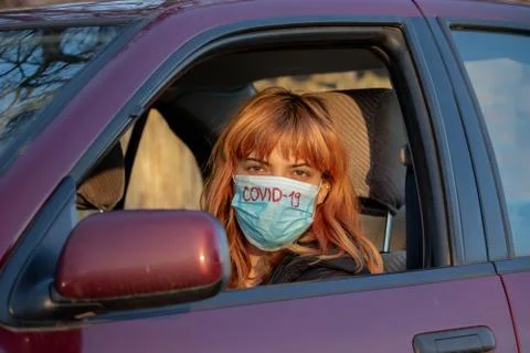Girl wearing medical mask in the car. Woman wearing mask, written COVID-19, t Stock Photos