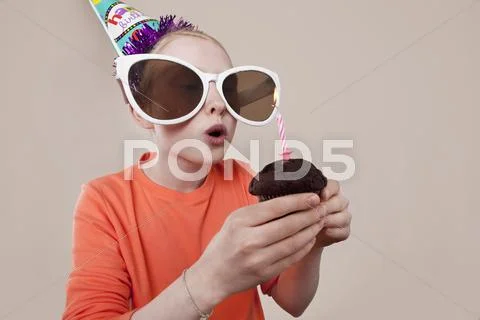 A girl wearing novelty sunglasses and party hat blowing out birthday candle Stock Photos