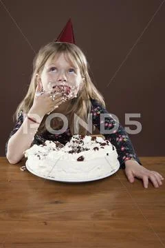 A girl wearing a party hat eating pie with her hands, studio shot Stock Photos