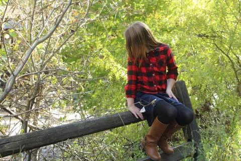 Girl wearing plaid and skirt sitting on fence looking at stream in Missoula M Stock Photos