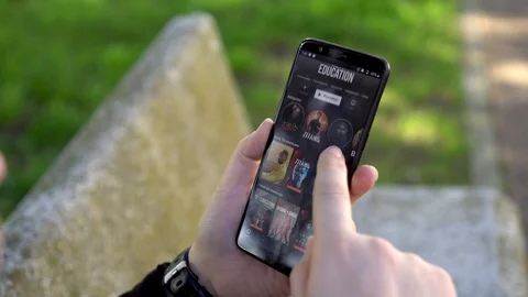A girl, while waiting sitting in the park, looks Netflix app. Stock Footage 123355205