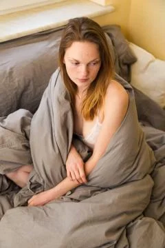 Girl in white bra sits in bed wrapped in blanket Stock Photos