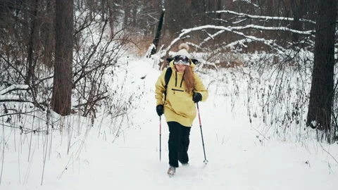 Girl with a white hat in the forest with a backpack and hiking sticks in winter Stock Footage 144693440