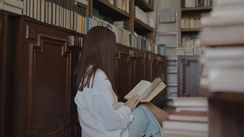 The girl in the white shirt is reading a book in the library Stock Footage 252040053