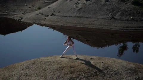 A girl in a white suit performs side lunges by the lake Stock Footage 134661884