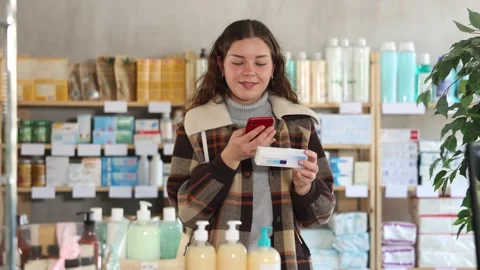 Girl in winter clothes scans code on package of ointment to check the expiration Stock Footage 309523701