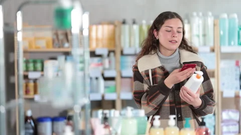 Girl in winter clothes scans code on package of cream to check the expiration Stock Footage 341427605