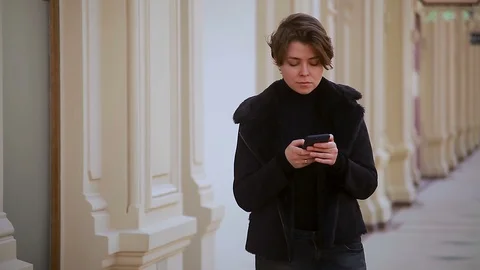 A girl in a winter jacket writes a message on her phone, interior Stock Footage 114229278