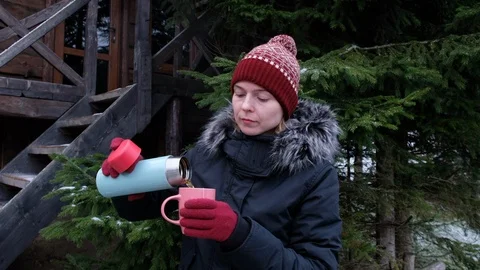 Girl in winter in a red hat drinking tea from a thermos against the background Stock Footage 102789629