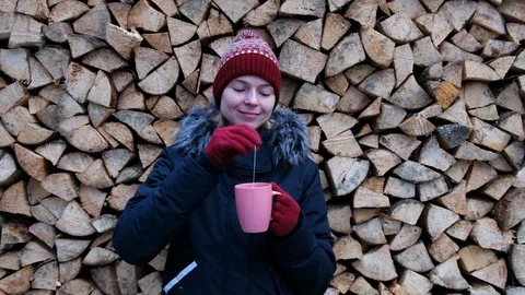 Girl in winter in red hat is drinking tea against the background of firewood. Stock Footage 102865174